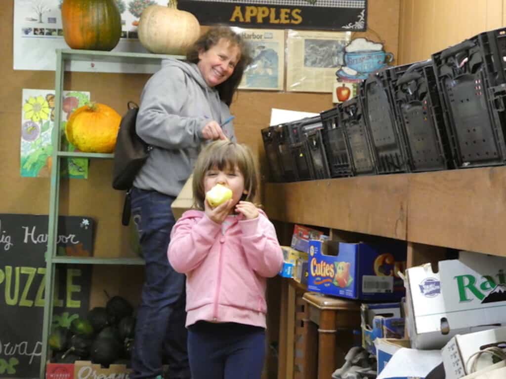  Three-year old Iselin Cabanas samples a “Blondie” apple as her mom, Kirsten Cabanas, fills a bag with this week’s load of apples from Butler’s Apple Farm. They make the trek from Roy every week to buy big bagfulls of Butler’s apples.