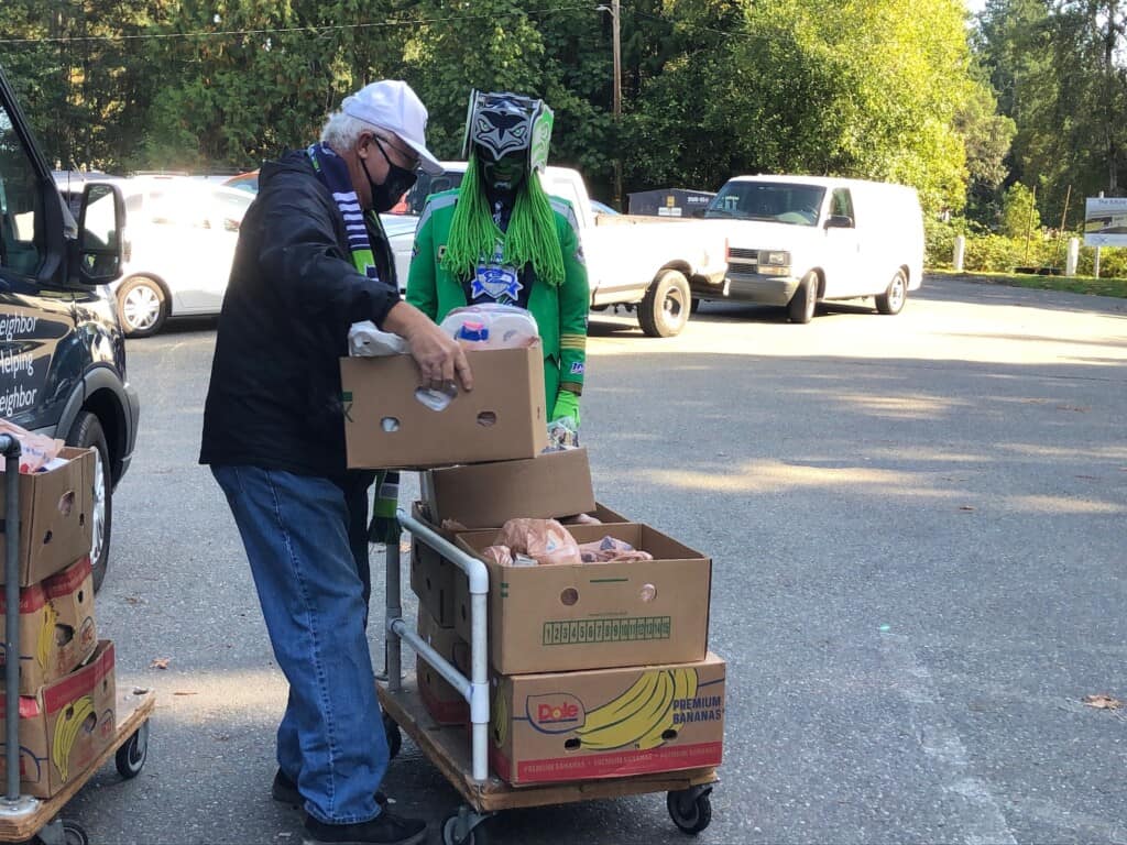 FISH volunteer Kevin Cummings helps Capt. Seahawk load up a cart with food donations. The captain visited FISH recently to announce that he plans to give a donation to the organization.