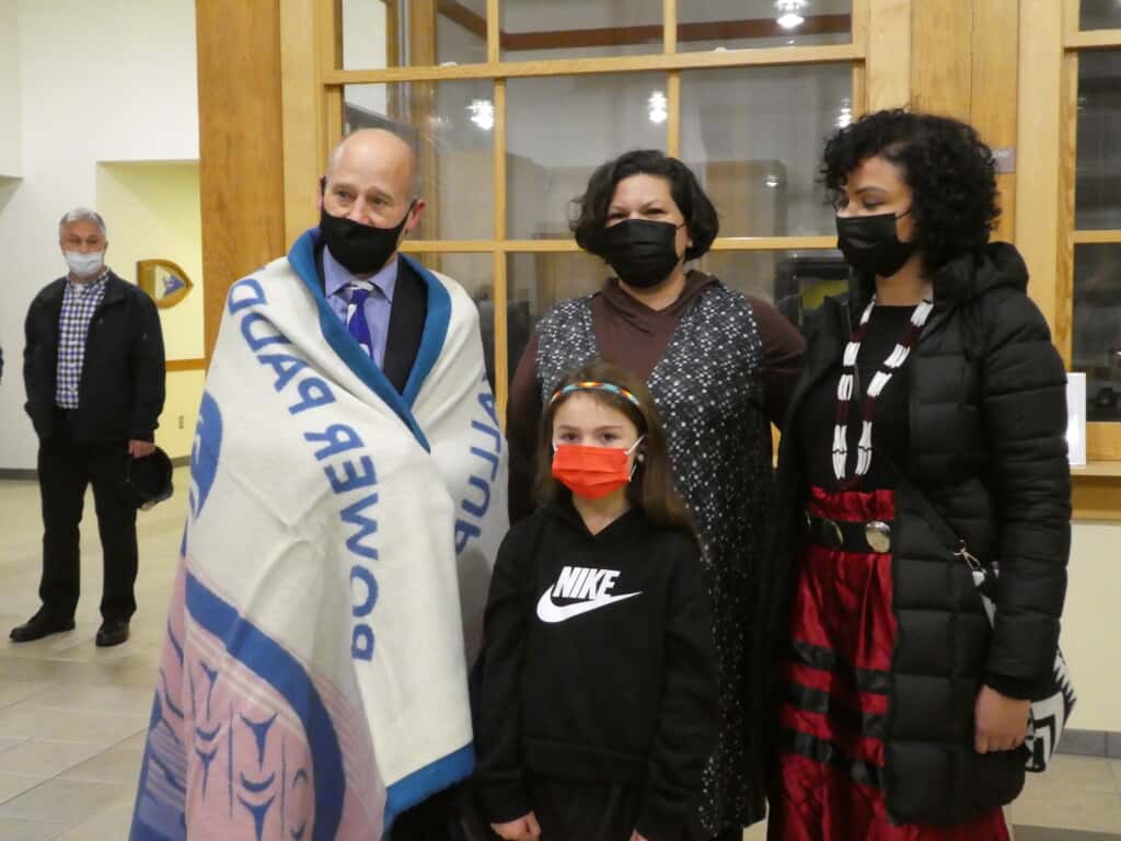 Mayor Kit Kuhn wrapped in the blanket presented to him by Puyallup Tribal Councilmember Anna Bean, Tribal Language Program Director Amber Hayward and six-year old Tribal member Zoe Keating