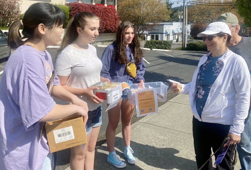 Gig Harbor High School Chinese language students (from left) Anna Daetwiler, Kaitlyn Stefanski and Mia Morente speak to passers-by to raise awareness of possible cuts in the program on Sunday, April 24, 2022, in downtown Gig Harbor.