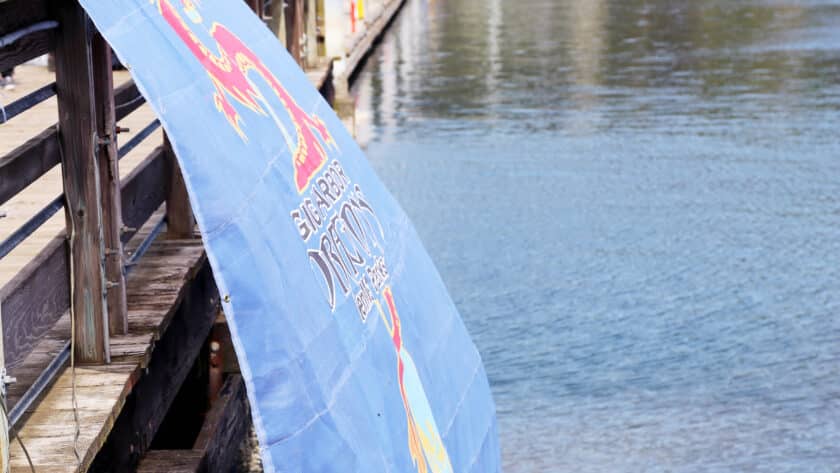 A Dragon Boats banner billows in the breeze while paddlers board their boats.