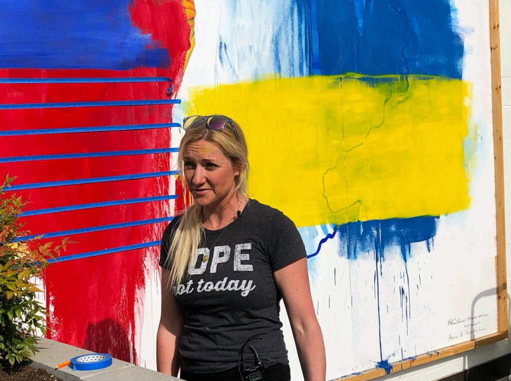 Artist Hillarie Isackson paints over the damage to the mural she painted in support of Ukraine near her gallery on North Harborview Drive.