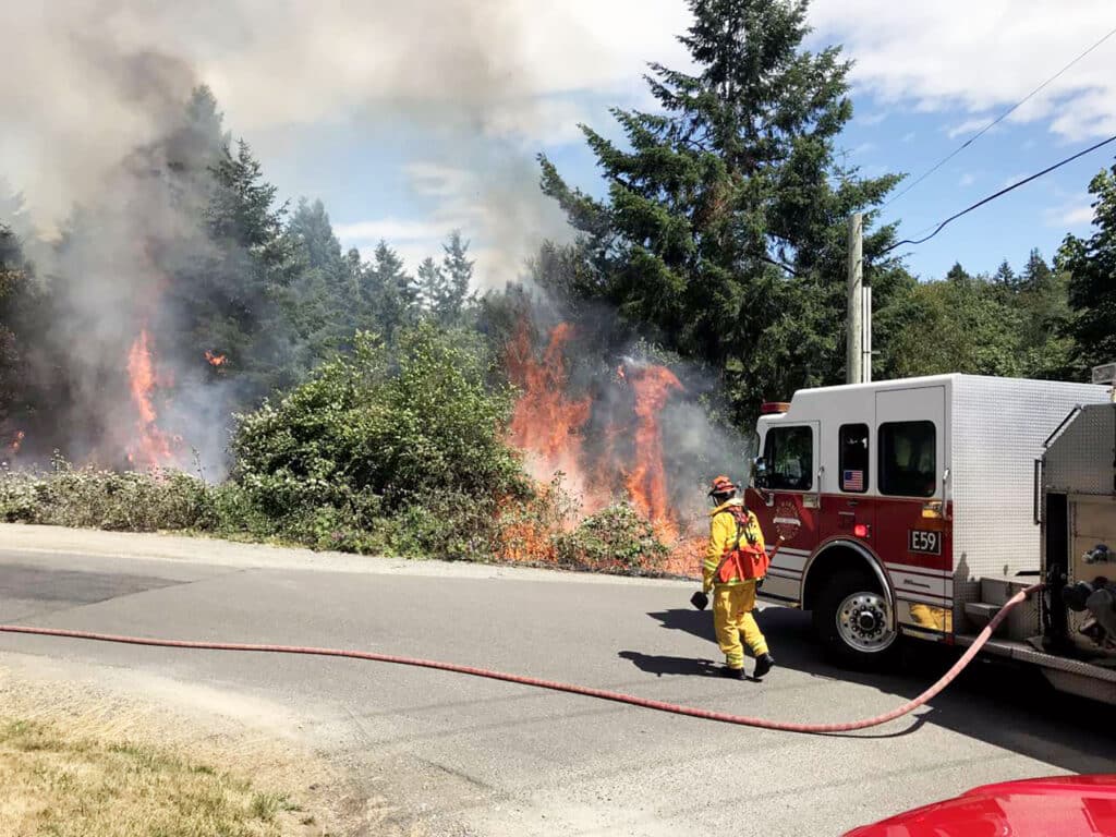 A fire crew from Gig Harbor Fire & Medic One fights a brush fire in 2019 at Murphy Drive and East Bay Drive.