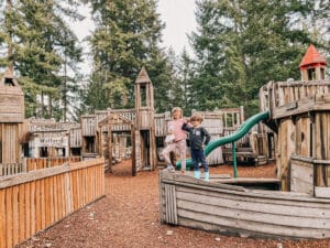 Two kids stand on wooden boat climber at playground