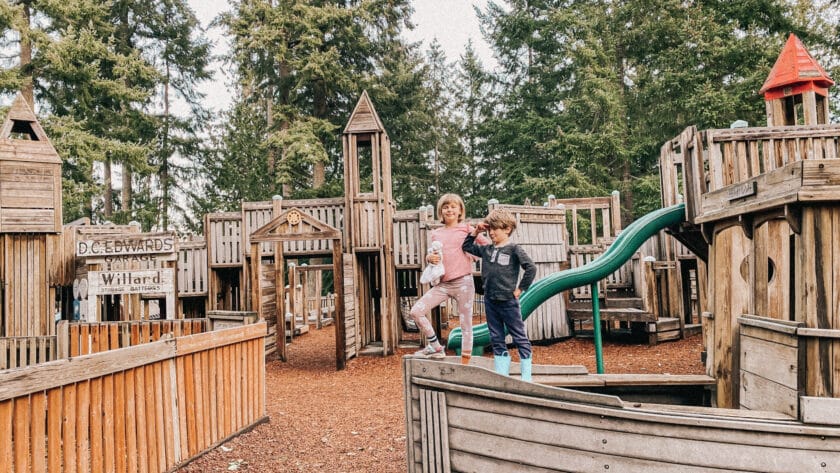 Two kids stand on wooden boat climber at playground