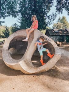 Two children sit on a concrete sculpture shaped like a snail shell.