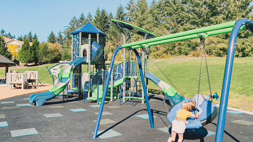 This is a photo of a blue and green playground equipment including a tower slide and disc swings