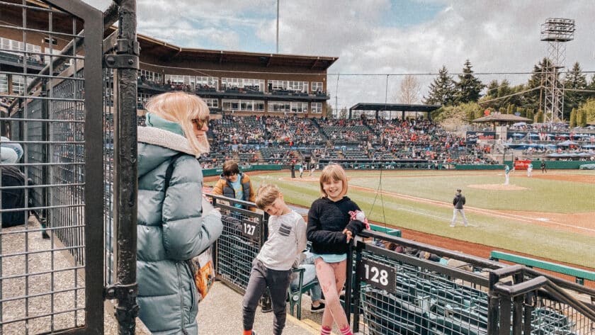 This is a photo of a mom and two kids a standing up in the stands of a baseball stadium posing for a camera.