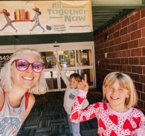 mom and two kids under yellow banner at library entrance