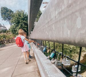 A boy and girl look at many padlocks hanging from a bridge railing