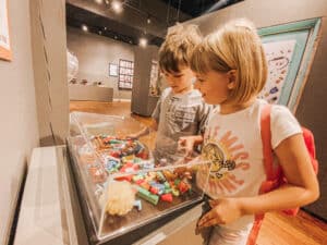A boy and a girl looking at toys behind glass at a museum.