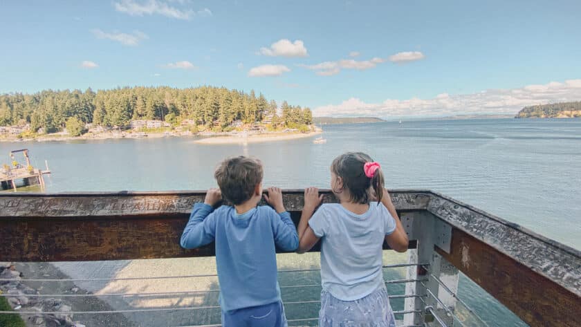 This is a photo of two kids posing behind a wooden railing above the water.