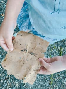 This is a photo of a little girl looking at a brown piece of paper she found on a sandy beach. She unfolded the worn paper and it has torn edges.