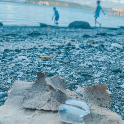 This is a photo of a brown piece of paper closeup on the sand and small rocks with kids playing in the background.